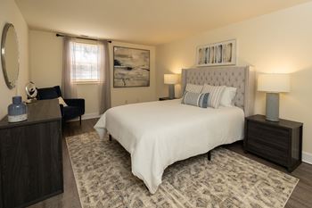 A bedroom with a large bed, a nightstand, and a chair at Hyde Park Apartments*, Essex, MD 21221